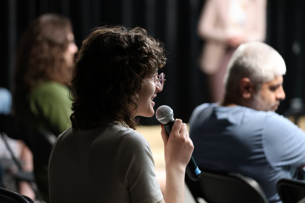Annie holds a microphone in the crowd, asking a question.