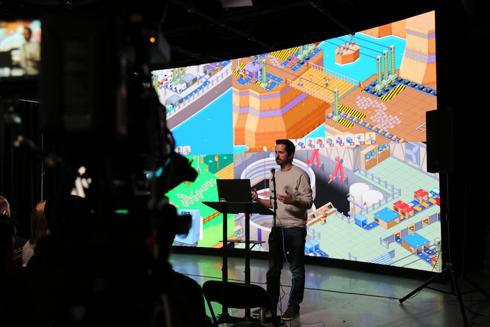 Kyle Schmitz presents in front of a camera and the LED wall about his game, Little Rocket Lab.